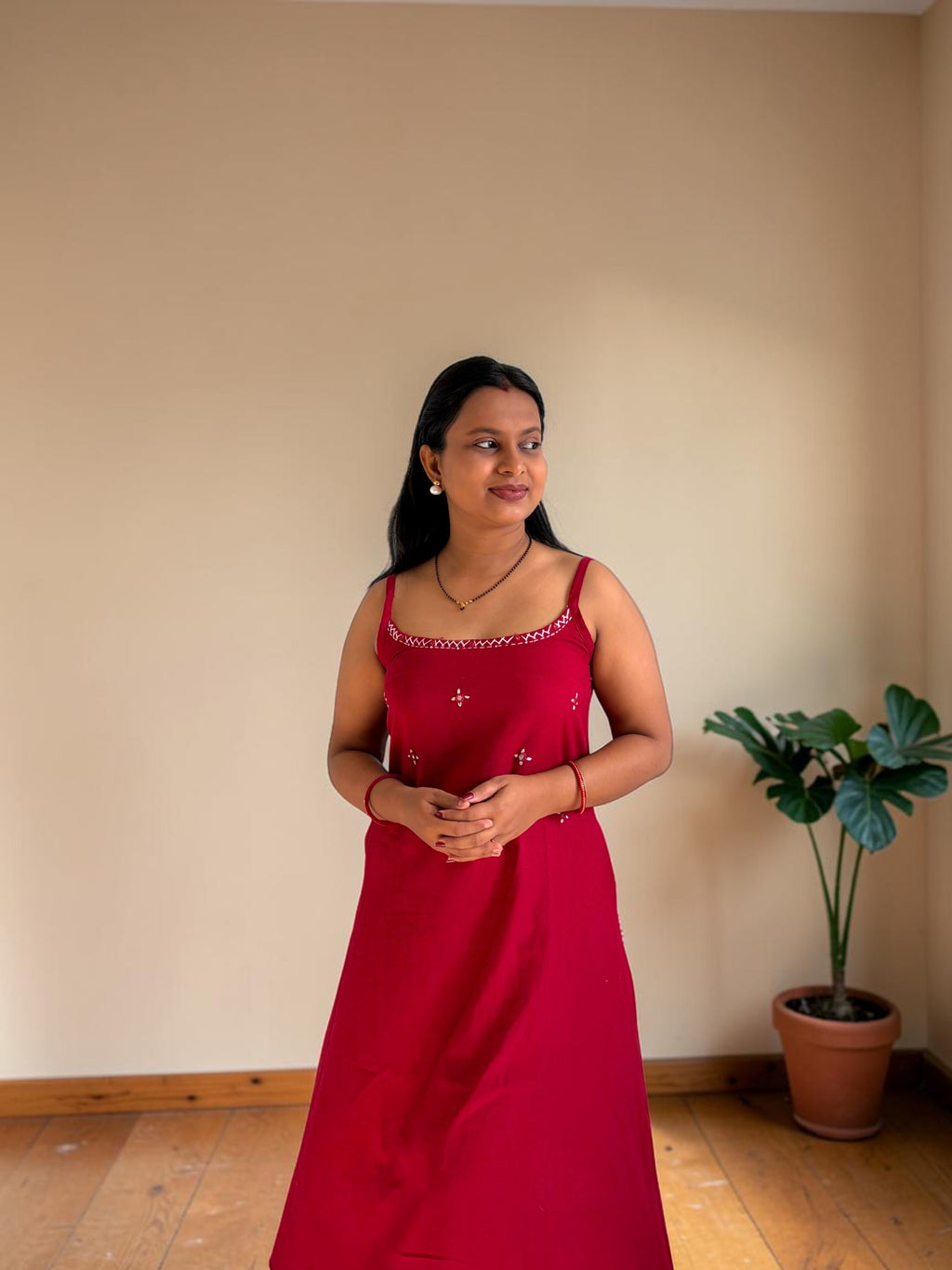 Woman in a red dress standing in a room with a plant in the corner.