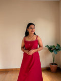Woman in a red dress standing in a room with a plant in the corner.