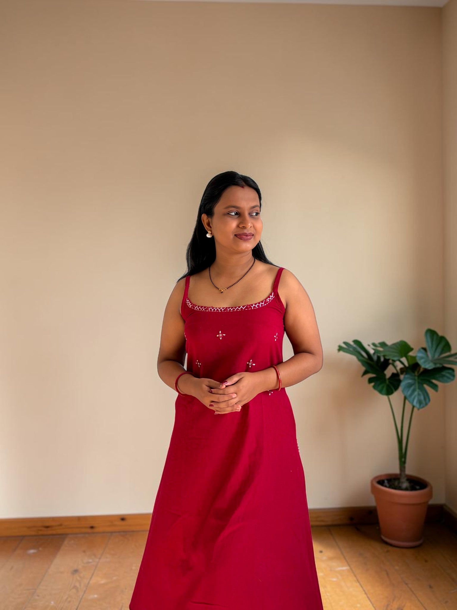 Woman in a red dress standing in a room with a plant in the corner.